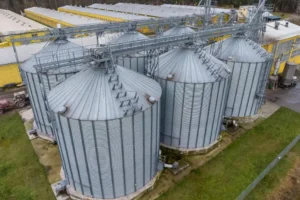 Sustentabilidade no agronegócio: o papel do GLP no campo sustentabilidade no agronegócio: Vista aérea de silos metálicos em uma unidade de armazenamento agrícola, com estrutura industrial e telhados ao fundo, em ambiente externo no campo.