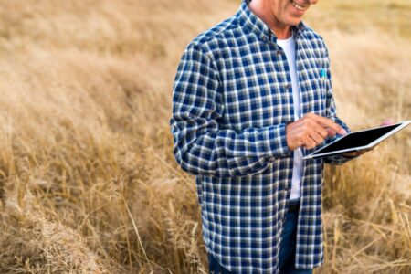 Homem com camisa xadrez usa tablet em um campo com grama seca