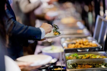 Pessoa servindo-se em um buffet com diversas opções de comida quente, em um evento ou ambiente formal