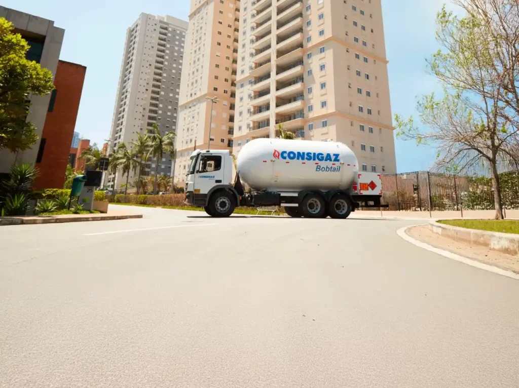 Instalação de gás encanado em condomínio: guia prático Caminhão de transporte de gás com tanque da Consigaz e inscrição Bóbtail estacionado em frente a prédio residencial, mostrando apoio à instalação de gás encanado em edifícios.