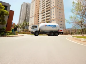 Instalação de gás encanado em condomínio: guia prático Caminhão de transporte de gás com tanque da Consigaz e inscrição Bóbtail estacionado em frente a prédio residencial, mostrando apoio à instalação de gás encanado em edifícios.