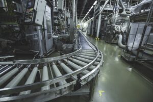 Imagem de uma fábrica moderna com linha de produção automatizada, incluindo esteiras transportadoras em operação, otimizada para indústria e manufatura.