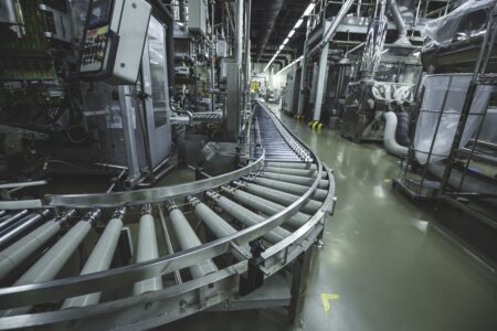 Imagem de uma fábrica moderna com linha de produção automatizada, incluindo esteiras transportadoras em operação, otimizada para indústria e manufatura.