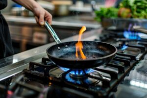 Pessoa acende o fogo no fogão usando uma frigideira preta, preparando uma receita na cozinha com o fogo acessa e uma chama visível. Ambiente de cozinha moderna, com foco na segurança alimentar.
