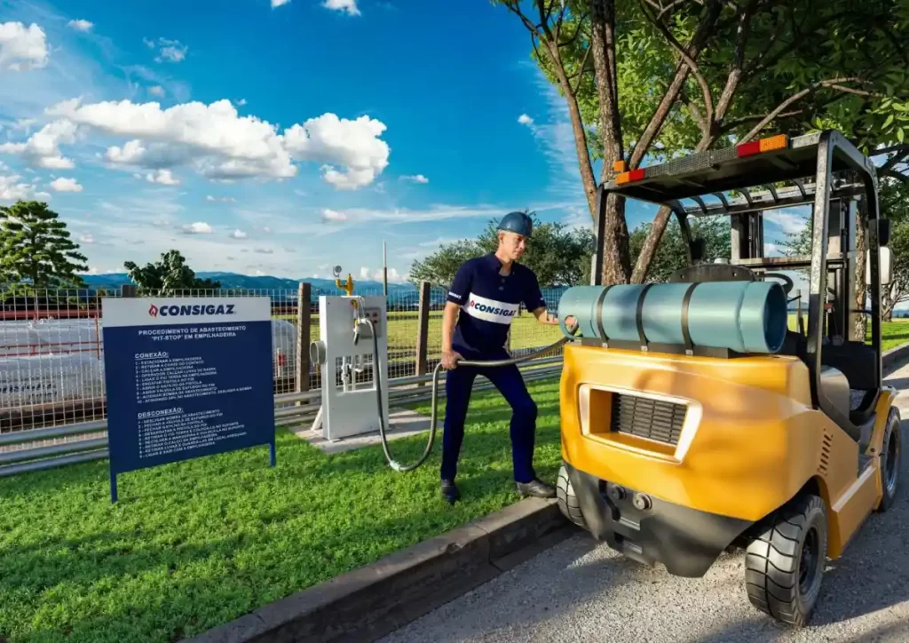 Profissional da Consigaz operando e abastecendo com GLP para empilhadeira em área externa com árvores e céu azul ao fundo.